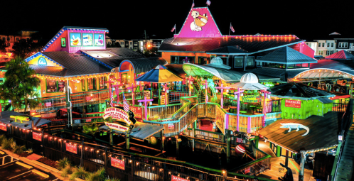 Colorful, illuminated restaurant and entertainment complex at night, featuring vibrant decor and outdoor seating areas.