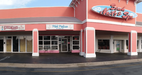 Exterior of a pink-themed shopping plaza featuring "Island Pizza" and "Pink Pelican" storefronts.
