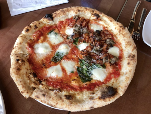 A freshly baked pizza with mozzarella, tomato sauce, spinach, and various toppings, served on a wooden table.