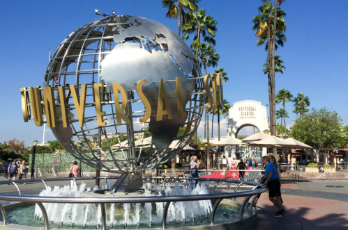 A large metallic globe with "UNIVERSAL" in gold, surrounded by palm trees and visitors at Universal Studios.