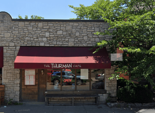A stone building with a red awning reading "The Thurman Cafe" and an "Open" sign in the window.