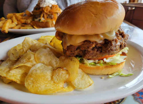 A juicy burger with melted cheese, lettuce, and tomato, served with a side of crispy potato chips.
