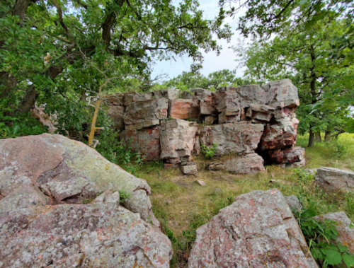 A rocky outcrop surrounded by greenery, featuring large, weathered stones and patches of grass.