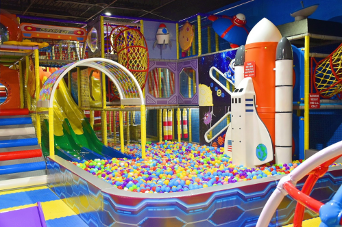 Colorful indoor play area featuring a slide, ball pit, and rocket-themed structures for children.
