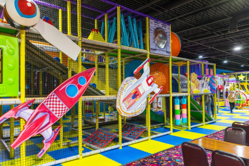 Colorful indoor playground with climbing structures, slides, and play equipment, featuring a space theme and vibrant flooring.