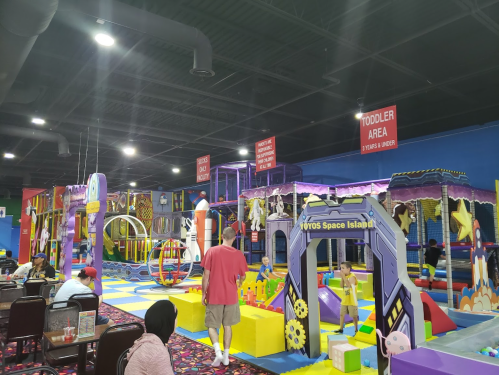 A colorful indoor play area with various structures for children, including a toddler zone and seating for parents.