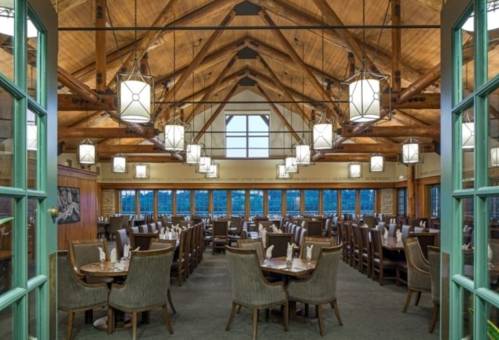 A spacious restaurant interior with wooden beams, large windows, and tables set for dining under hanging lanterns.