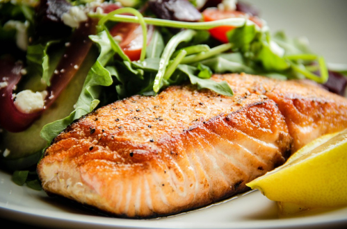A perfectly cooked salmon fillet served with a fresh salad and a slice of lemon on a white plate.