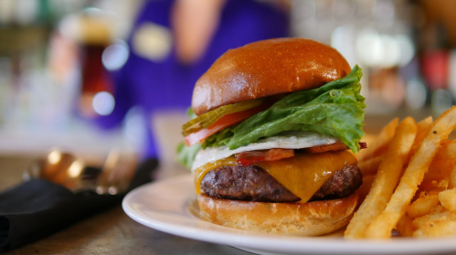 A juicy cheeseburger with lettuce, tomato, and pickles, served with crispy fries on a white plate.