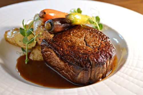 A perfectly cooked steak with a rich sauce, accompanied by roasted potatoes and colorful baby carrots on a white plate.