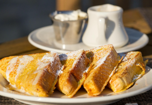 A plate of golden French toast dusted with powdered sugar, served with a small cup of cream.