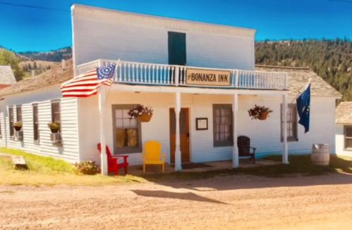 A historic building with a sign reading "Bonanza Inn," featuring flags and colorful chairs on the porch.