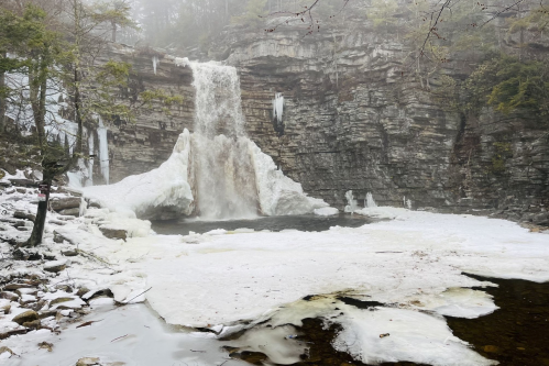 A frozen waterfall cascading over rocky cliffs, surrounded by ice and misty winter scenery.