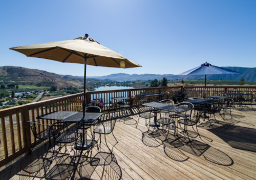A sunny outdoor deck with tables and umbrellas overlooking a scenic landscape and water.