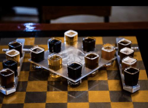 A chessboard with shot glasses filled with various colored liquids arranged in a strategic pattern.