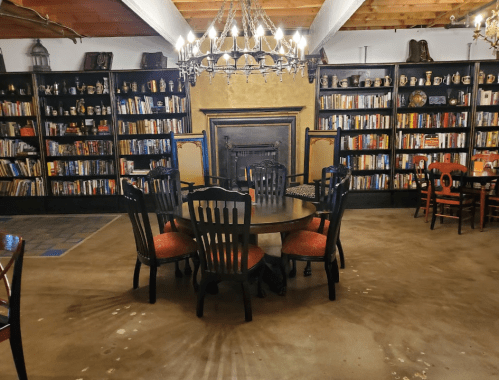 Cozy library with dark wooden shelves filled with books, a round table, and chairs under a chandelier.