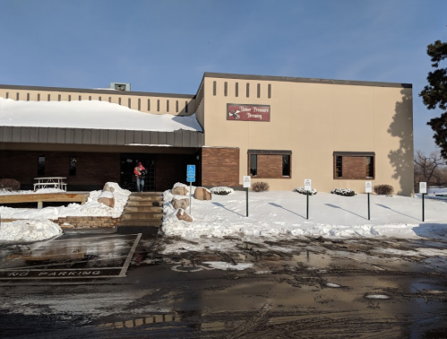 A building with a sign reading "Senior Center" surrounded by snow, with a person exiting and parking signs visible.