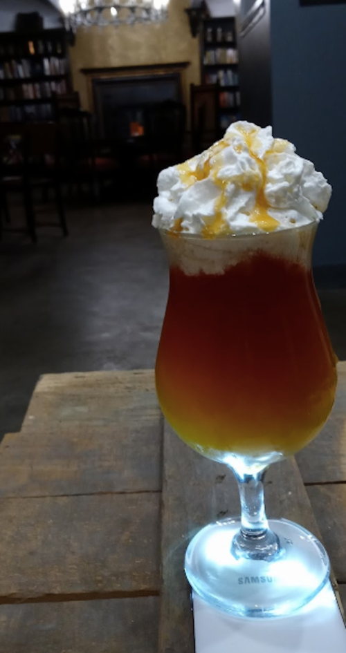 A colorful layered drink topped with whipped cream and caramel, served in a tall glass on a wooden table.