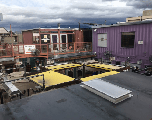 A view of a colorful shipping container complex with outdoor seating and a cloudy sky in the background.