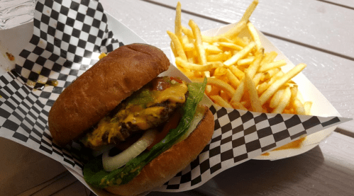 A juicy cheeseburger with lettuce, tomato, and onion, served with a side of crispy French fries in a checkered container.