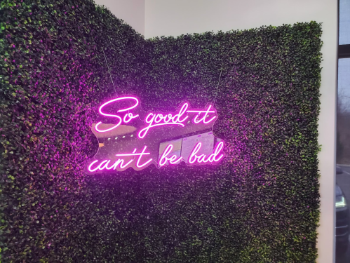 Neon sign on a green wall reads, "So good, it can't be bad."