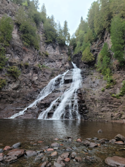 A serene waterfall cascading down rocky cliffs, surrounded by lush green trees and a calm pool at the base.
