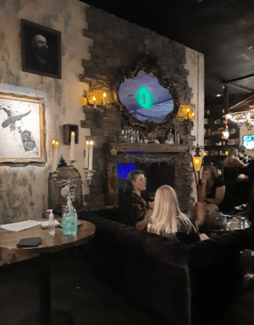 A cozy bar scene with people chatting, a stone fireplace, candles, and a large mirror reflecting an eerie eye.