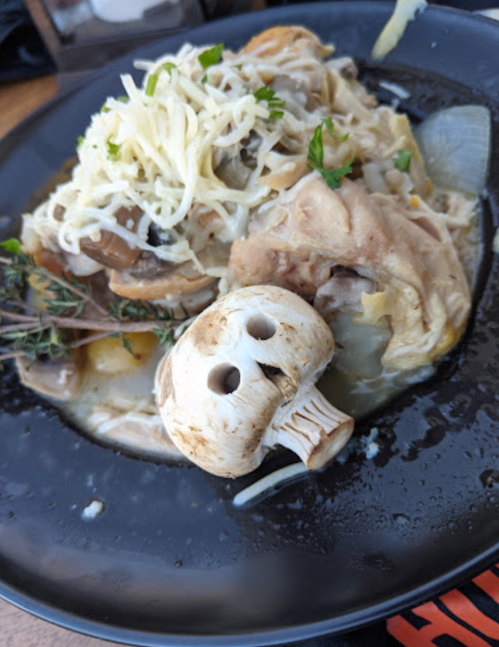 A plate of chicken and vegetables topped with cheese, accompanied by a decorative mushroom on the side.