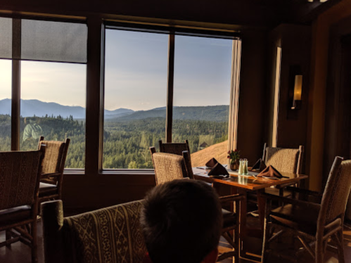 A cozy restaurant with wooden chairs, featuring large windows showcasing a scenic mountain view.