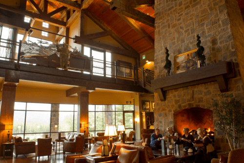 Cozy lodge interior with a stone fireplace, wooden beams, and guests enjoying drinks in a warm, inviting atmosphere.