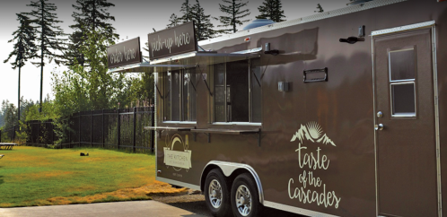 A food truck named "Taste of the Cascades" parked in a grassy area with trees in the background.