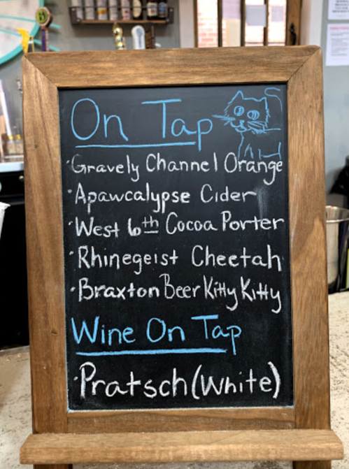 A chalkboard menu listing beers on tap, including Gravely Channel Orange and Apawcalypse Cider, plus a white wine option.