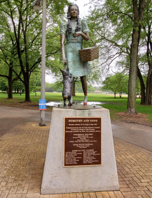 Statue of Dorothy and Toto in a park, with a plaque detailing its dedication and community contributions.