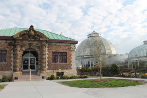 Historic aquarium building with a green roof, surrounded by large glass conservatories and landscaped gardens.