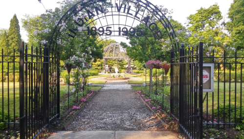 A garden entrance with an archway reading "Illiana Village" and a pathway leading to a landscaped area with flowers.