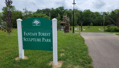 Sign for Fantasy Forest Sculpture Park, with a pathway and sculptures visible in a green, grassy area.