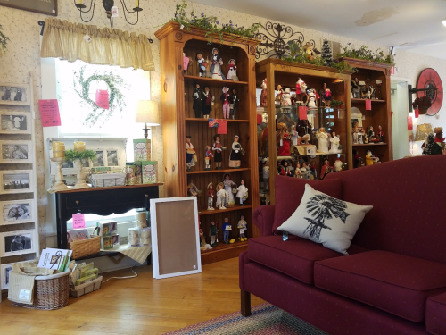 A cozy shop interior featuring a red couch, wooden shelves filled with collectibles, and decorative items.
