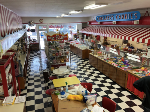 A colorful candy shop interior with checkered floors, display cases filled with sweets, and a seating area.