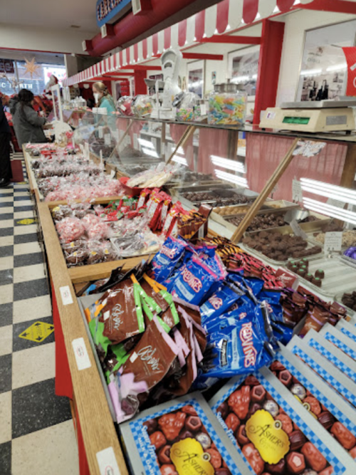 A colorful candy shop display with various sweets, chocolates, and treats in glass cases and on wooden counters.
