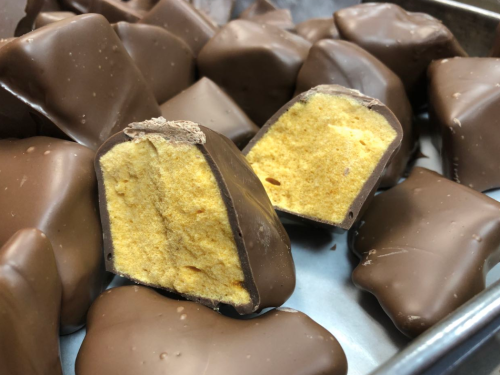A close-up of chocolate-covered treats, some whole and one cut in half, revealing a yellow filling inside.