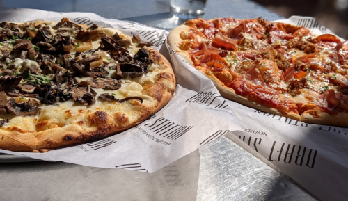 Two pizzas on a table: one topped with mushrooms and cheese, the other with pepperoni and sausage, both on parchment paper.
