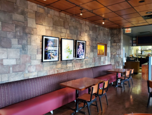 Interior of a restaurant featuring a stone wall, framed artwork, and wooden tables with chairs.