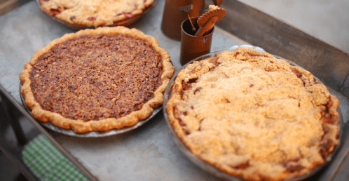 Two freshly baked pies on a tray: one with a crumbly topping and the other with a glossy, nutty filling.