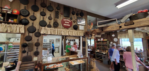 A rustic shop interior with cast iron pans on the wall, a bakery display, and customers browsing.