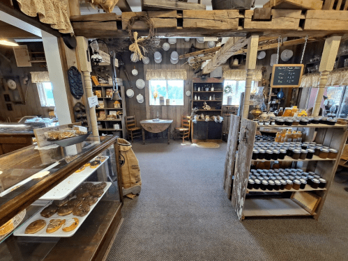 Cozy interior of a rustic shop featuring shelves of jars, baked goods, and wooden decor. Warm, inviting atmosphere.