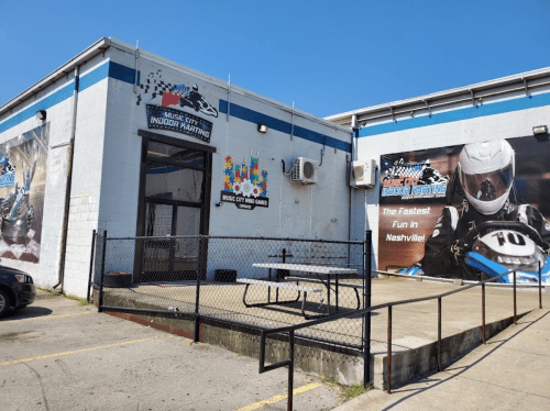 Exterior of Music City Indoor Karting, featuring a racing-themed mural and a fenced area with a table.