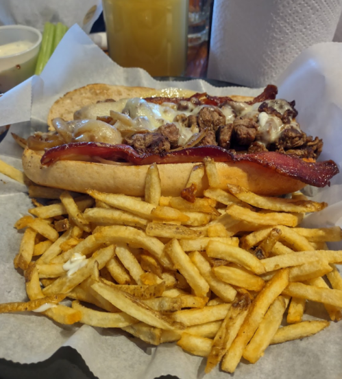 A loaded sandwich with grilled meat, cheese, and bacon, served with a side of crispy French fries.
