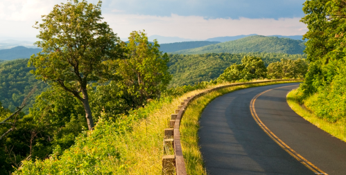 A winding road curves through lush green hills under a partly cloudy sky.