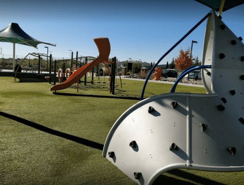 A colorful playground with climbing structures and slides on green turf under a clear blue sky.
