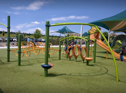 Colorful playground equipment with slides, climbing structures, and swings on green grass under a blue sky.